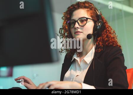 Porträt einer schönen jungen Frau Operator mit roten Locken Haare und Gläser im Inneren des Callcenters Office arbeitet am Computer und nutzt Stockfoto