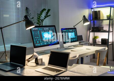 Leeres zeitgenössisches Büro der Autodesignfirma mit Automobilbildern auf Computermonitoren auf mit Lampen beleuchteten Tischen Stockfoto