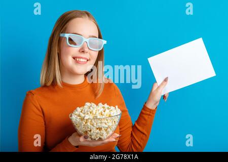 Emotionales Porträt einer jungen Frau in einer Kinobrille. Lächelndes Teenager Mädchen Filmbetrachter in Gläsern halten Popcorn und Ekty weißen Blanc Karte für Spott Stockfoto