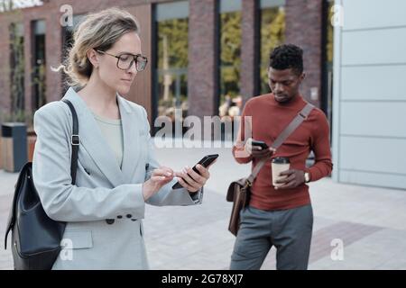 Blonde Geschäftsfrau mit Smartphone-SMS gegen afrikanischen Mann Stockfoto