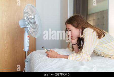 Teenager liegt mit dem Telefon vor dem Kühlgebläse. Stockfoto