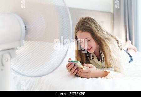 Teenager liegt mit dem Telefon vor dem Kühlgebläse. Stockfoto