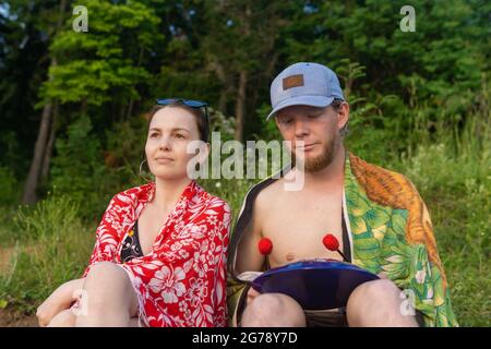 Region Perm, Russland - 27. Juni 2021: Ein paar junge Leute sitzen draußen, ein Mann spielt auf einer hank-Trommel Stockfoto