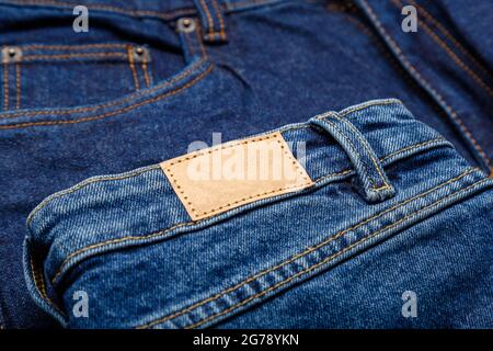 Jeans in blauer Denim mit Emty-Label. Braunes lederfarbenes Label-Tag auf Denim-Hosen-Hintergrund. Leeres Mockup-Etikett in beigem Leder. Nahaufnahme Stockfoto