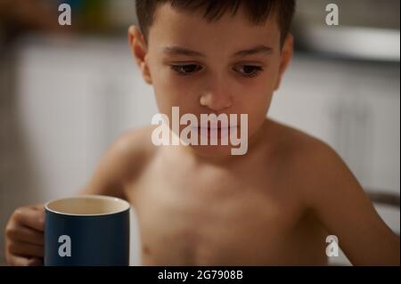 Kopfbild eines entzückenden Jungen mit einer Keramikschale mit heißem Getränk Stockfoto