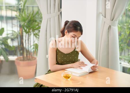 Schöne fröhliche junge Mädchen sitzt am Küchentisch, Notizen in einem Tagebuch Stockfoto