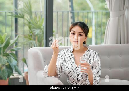 Glückliche Frau unter einem Vitamin-gelben Pille auf einer Couch im Wohnzimmer zu Hause sitzen Stockfoto
