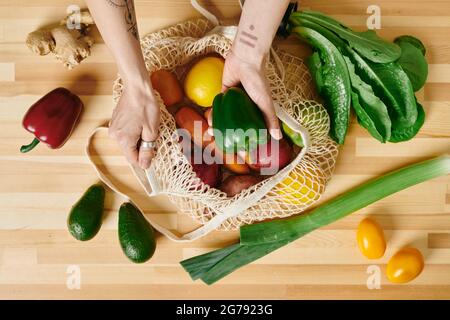 Hände einer jungen Frau, die frisches Gemüse aus dem Beutel nimmt, während sie Salat kocht Stockfoto