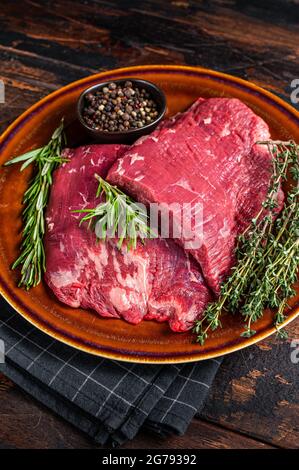 Zwei Lappen oder Flanken rohes Rindfleisch Steaks auf einem rustikalen Teller mit Kräutern. Dunkler Holzhintergrund. Draufsicht Stockfoto