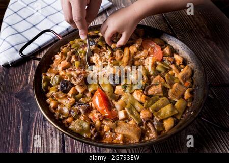Die Hand eines Mannes und die Hand eines Kindes schmecken Paella. Zeit, um mit Papa in der Küche zu teilen Stockfoto
