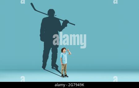 Kindheit und Traum von der großen und berühmten Zukunft. Konzeptuelles Bild mit Jungen und Schatten eines fitgen männlichen Eishockeyspielers auf blauem Hintergrund Stockfoto