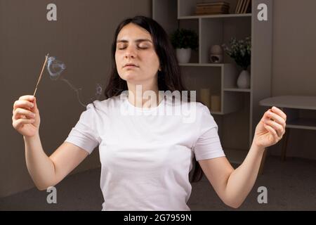 Ein aromatischer Indianerstab brennt, die Frau im Hintergrund meditiert. Aromatherapie, Selbsteintauchen, die Kraft des Denkens Stockfoto