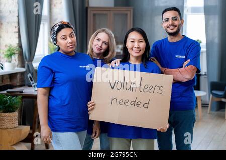 Vier junge, multirassische Freiwillige in blauen T-Shirts stehen in häuslicher Umgebung Stockfoto