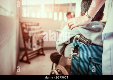 Krankenschwester, die den Rollstuhl mit dem Patienten schiebt. Junge Jugendliche Behinderte, die im Rollstuhl sitzen. Lähmung und Beeinträchtigung im wirklichen Leben. Stockfoto