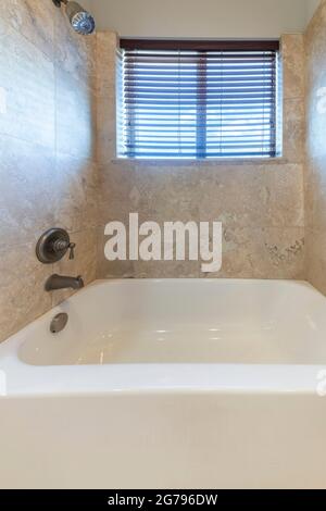 Kleines Badezimmer mit Keramikbadewanne und einem an der Wand montierten Duschkopf und Wasserhahn Stockfoto