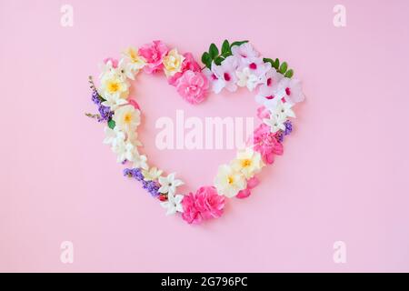 Schöne herzförmige, Rahmenzusammensetzung, verschiedene frische Blumen auf rosa Hintergrund.Copy space.Valentines, Mütter, Frauen Tag Concept.Flat Lay, Draufsicht.Template, Design von Hochzeitseinladungen, Karten. Stockfoto