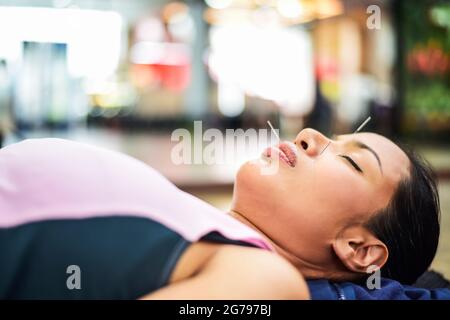 Im selektiven Fokus auf verschwommen von Hand Durchführung Akupunkturtherapie auf Kundengesicht.Cross-Verarbeitung und Split-Ton neue Farbtrend wie Prozess. Stockfoto