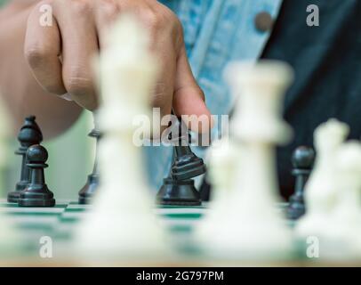 Schachspiel auf einem grünen Brett hält eine Hand einen schwarzen Bauer Stockfoto