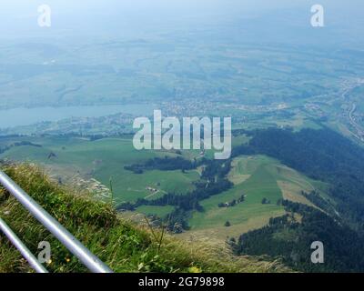 Blick von einem Berg ins Tal. Sie können einen See, ein Dorf, sowie große grüne Wiesen und einige Waldgebiete sehen Stockfoto