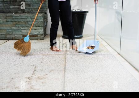 Menschen, Hausarbeit, Reinigung und Housekeeping-Konzept - Nahaufnahme von Frauenbeinen mit Besen, die den Balkonboden zu Hause fegen Stockfoto