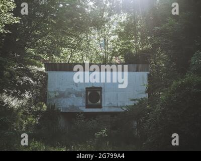 Ein verlassene Betongebäude mit kreisförmigem Lüftungsschacht in einem Walddickicht mit Sonnenstrahlen, die durch das Laub scheinen. Fine Noise künstlerische Proc Stockfoto