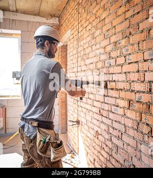 Handwerker auf einer Baustelle, der gerade eine Wand mit einem Perforator bohrt. Stockfoto