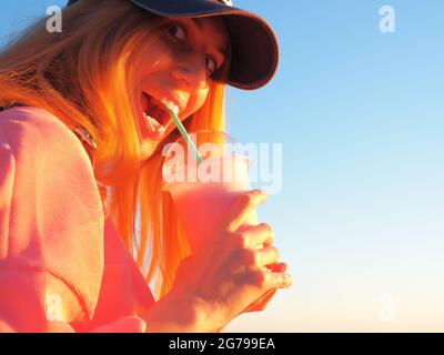 Mädchen mit prall gefüllten Augen und ihrem Mund hält Glas mit einem milchig rosa Cocktail in den Händen Stockfoto