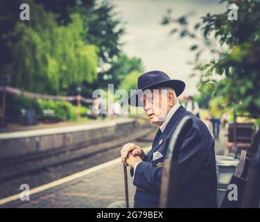 Nahaufnahme eines elegant gekleideten, älteren Herrn in 1940 Kostümen, der isoliert auf einer Bahnsteigsbank, Severn Valley Railway Arley Station, Veranstaltung aus den 1940er Jahren des 2. Weltkriegs, sitzt. Stockfoto