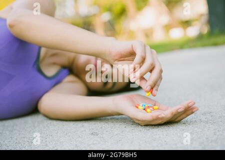 Verrückt in schlanken jungen Frauen in Sportkleidung fallen auf Bürgersteig versuchen, viele Pillen in der Hand zu essen.dramatische Moment. Stockfoto