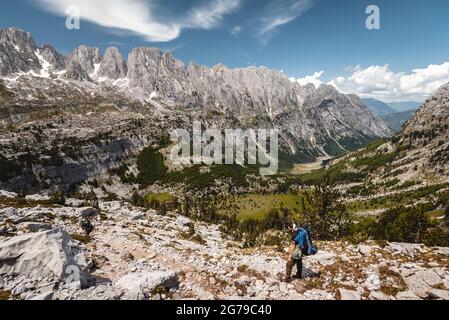 Bei strahlendem Sonnenschein blickt ein einziger Wanderer über die Landschaft des Prokletije-Nationalparks zu einem riesigen Bergmassiv, Albanien Stockfoto