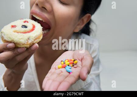 Im selektiven Fokus der verrückten Frauen essen Lächeln Donut mit halten viele Pillen in der Hand.dramatische Moment. Stockfoto