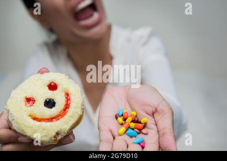 Im selektiven Fokus der verrückten Frauen essen Lächeln Donut mit halten viele Pillen in der Hand.dramatische Moment. Stockfoto