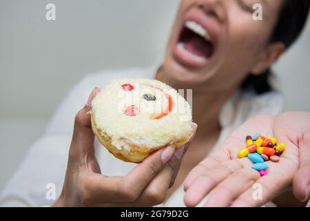 Im selektiven Fokus der verrückten Frauen essen Lächeln Donut mit halten viele Pillen in der Hand.dramatische Moment. Stockfoto