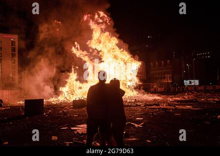 Belfast, Großbritannien. Juli 2021. Ein Paar beobachtet das Lagerfeuer bei den Feierlichkeiten der elften Nacht in Sandy Row, Belfast. Um die Schlacht von Boyne zu feiern, werden in verschiedenen protestantischen Vierteln in Belfast Lagerfeuer errichtet und Straßen und Häuser mit Union Jacks geschmückt. Die Lagerfeuer werden in der Nacht vor den Paraden des 12. Juli, am 11. Juli, angezündet. (Foto von Natalia Campos/SOPA Images/Sipa USA) Quelle: SIPA USA/Alamy Live News Stockfoto