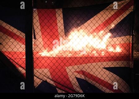 Belfast, Großbritannien. Juli 2021. Das Lagerfeuer der Sandy Row, das durch die britische Union Jack-Flagge bei den Feierlichkeiten der elften Nacht in Belfast gesehen wurde. Um die Schlacht von Boyne zu feiern, werden in verschiedenen protestantischen Vierteln in Belfast Lagerfeuer errichtet und Straßen und Häuser mit Union Jacks geschmückt. Die Lagerfeuer werden in der Nacht vor den Paraden des 12. Juli, am 11. Juli, angezündet. (Foto von Natalia Campos/SOPA Images/Sipa USA) Quelle: SIPA USA/Alamy Live News Stockfoto