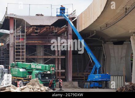 12. Juli 2021, Brandenburg, Potsdam: Ein Arbeiter steht auf einer Steigleitung an einem der Segmente der alten Brücke auf der Baustelle der Hochbrücke der Landstraße L40 Nuthestraße. Aufgrund von Platzmangel werden die rund 30 Meter langen und 600 Tonnen schweren Abschnitte aus Beton und Verstärkungsstahl in mehreren Teilschritten hinter dem Abutment der Friedrich-Engels-Straße mittels Hydraulik gezogen, wo der alte Überbau zerkleinert und abtransportiert wird. Die Sanierung der Hochstraßenbrücke soll im Oktober 2022 abgeschlossen werden. Foto: Soeren Stache/dpa-Zentralbild/ Stockfoto