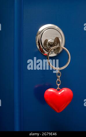 Hausschlüssel auf rotem herzförmigem Schlüsselanhänger im Türschloss Stockfoto