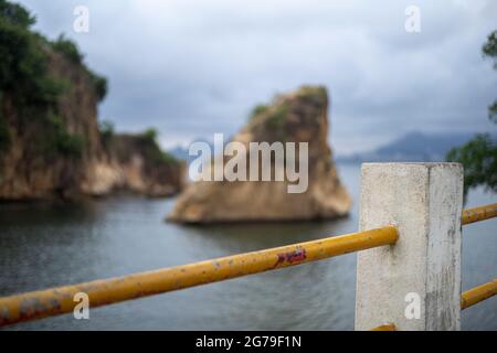 Der Blick von Ponte da Boa Viagem, Nitreói, Bundesstaat Rio de Janeiro, Brasilien. Grüne Ilha da Boa Viagem Privatinsel in Bucht, die über eine schmale Brücke und gelben Sand unter blauer Wolkenlandschaft mit dem Hauptland verbunden ist. Berge in der Ferne. Stockfoto