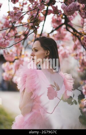 Schöne junge Frau in Rosenkleid in blühenden Sakura Garten. Stockfoto