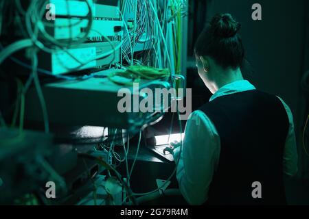 Rückansicht einer weiblichen Netzwerktechnikerin, die Server inspiziert, während sie mit Supercomputern im Rechenzentrum arbeitet, Kopierplatz Stockfoto