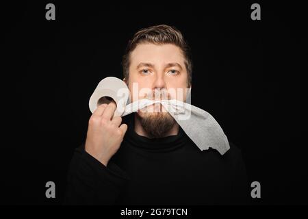 Mann, der Toilettenpapier isst. Lustige Hunger Mann, Fasten Konzept. Hungerstreik. Verrückter bärtiger Kerl. Schwarzer Hintergrund. Stockfoto