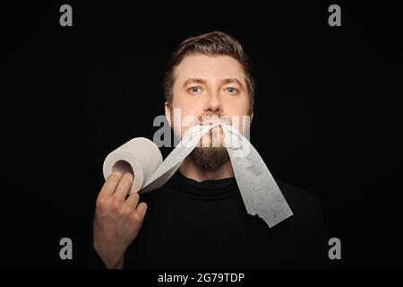 Mann, der Toilettenpapier isst. Lustige Hunger Mann, Fasten Konzept. Hungerstreik. Verrückter bärtiger Kerl. Schwarzer Hintergrund. Stockfoto