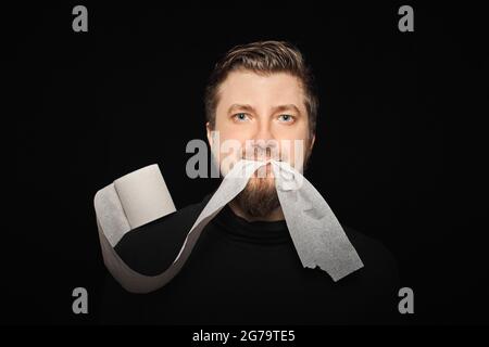 Mann, der Toilettenpapier isst. Lustige Hunger Mann, Fasten Konzept. Hungerstreik. Verrückter bärtiger Kerl. Schwarzer Hintergrund. Stockfoto
