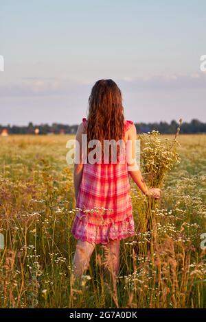 Vertikale Schuss zurück Ansicht junges Mädchen mit Blumen auf dem Feld. Stockfoto