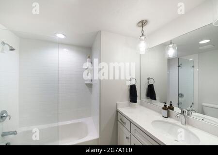 Kleines, modernes, schlichtes weißes Badezimmer mit einer Nische-Badewanne mit Glaswand und weißen Fliesen Stockfoto