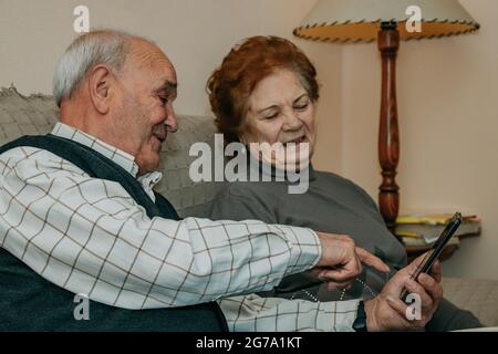 Seniorenpaar zu Hause mit Telefon und Buch auf dem Sofa Stockfoto