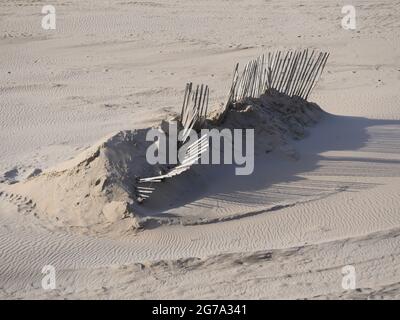 Ein gebrochener Holzzaun an einem Sandstrand, der in einem Sandhaufen vergraben ist. Das Holz gebleicht durch das Wetter. Der Sand ist feinkörnig Stockfoto