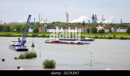 Duisburg, Nordrhein-Westfalen, Deutschland - Stadtlandschaft im Ruhrgebiet mit Frachtschiffen auf dem Rhein vor Wohngebäuden im Laar-Kreis und im hinteren Hochofen 8 des ThyssenKrupp Huettenwerks in Bruckhausen baggert vor dem Kranschiff den Rhein. Stockfoto