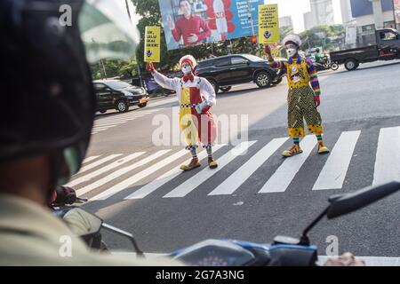 South Jakarta, Indonesien. Juli 2021. Mitglieder der Aku Badut Indonesian Community (ABI) in Clownkostümen zeigen Plakate, die das Tragen von Gesichtsmasken als Vorsichtsmaßnahme gegen die Verbreitung von Covid19 unterstützen. Mitglieder der Aku Badut Indonesia Community (ABI) gingen auf die Straße in Jakarta, um sich für die Umsetzung von Gesundheitsprotokollen während der Covid-19-Pandemie zu einsetzen. Kredit: SOPA Images Limited/Alamy Live Nachrichten Stockfoto