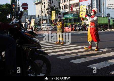 South Jakarta, Indonesien. Juli 2021. Mitglieder der Aku Badut Indonesian Community (ABI) in Clownkostümen zeigen Plakate, die das Tragen von Gesichtsmasken als Vorsichtsmaßnahme gegen die Verbreitung von Covid19 unterstützen. Mitglieder der Aku Badut Indonesia Community (ABI) gingen auf die Straße in Jakarta, um sich für die Umsetzung von Gesundheitsprotokollen während der Covid-19-Pandemie zu einsetzen. Kredit: SOPA Images Limited/Alamy Live Nachrichten Stockfoto